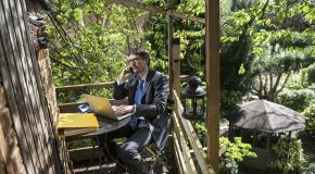 Persoon werkt op laptop en belt met gsm in een boomhut in groene omgeving